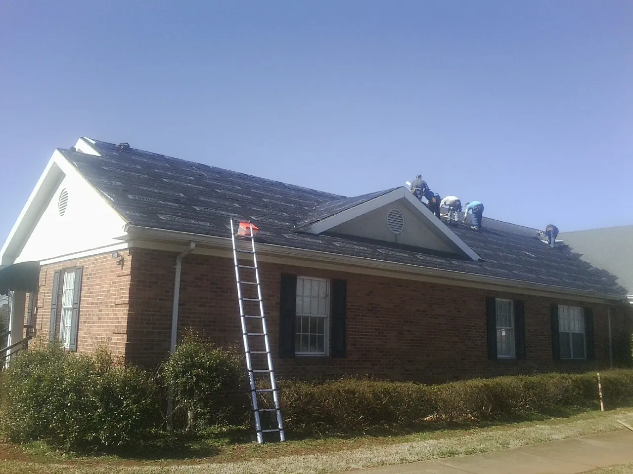 Crew tearing shingles off a brick ranch roof with a ladder set — Metal Roof Repair work by our crew in Hoffman