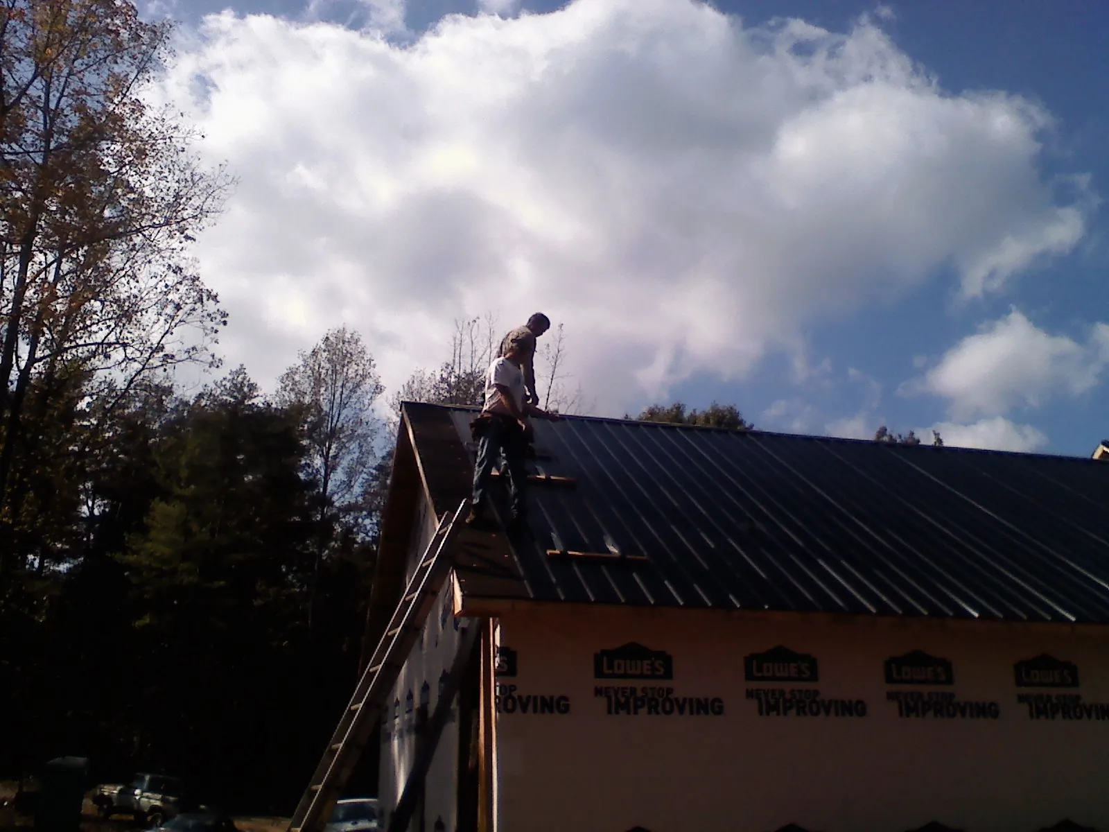 Roofer fastening dark metal panels high against a cloudy sky, from a Roof Inspection job in Hoffman